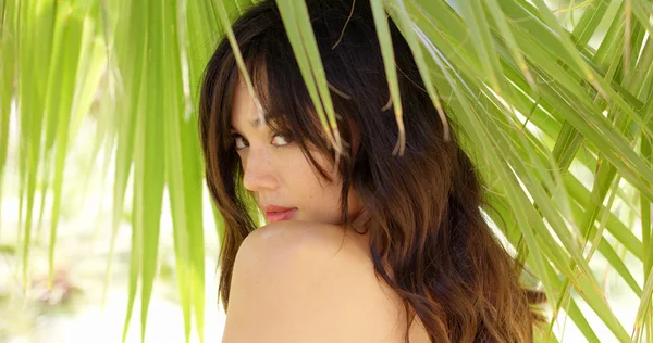 Shy young woman in shade of palm leaves