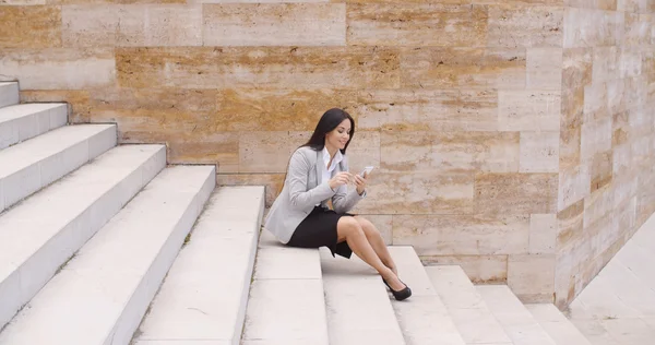 Businesswoman sitting on steps and using phone