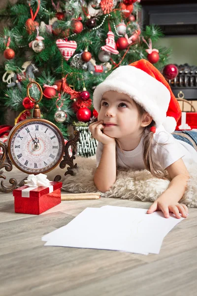 Dreaming little girl in Santa hat writes letter to Santa Claus