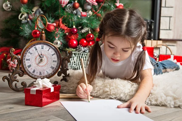 Pretty little girl in Santa hat writes letter to Santa