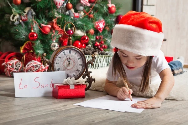 Pensive girl in Santa hat writes letter to Santa