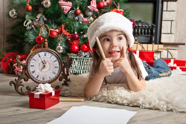 Thoughtful little girl in Santa hat writes letter to Santa Claus