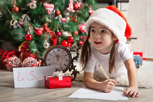 Pensive girl in Santa hat writes letter to Santa