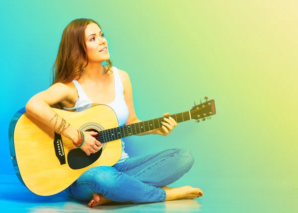 Woman musician with guitar sitting on a floor.