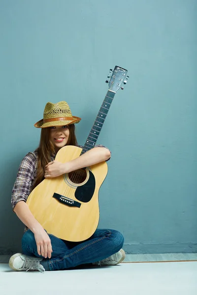 Girl seating on floor with acoustic guitar.