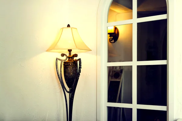 Antique brass floor lamp beside white wall and grille window