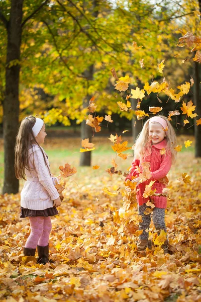 Two girls throwing leaves in autumn park