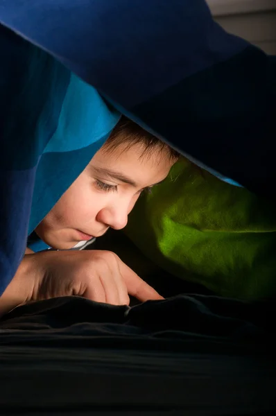 Boy reading a book under the covers