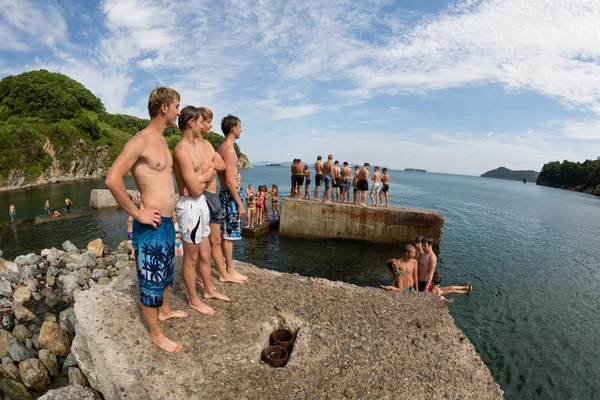 Joyful boy and girl jumping into the sea from old pier