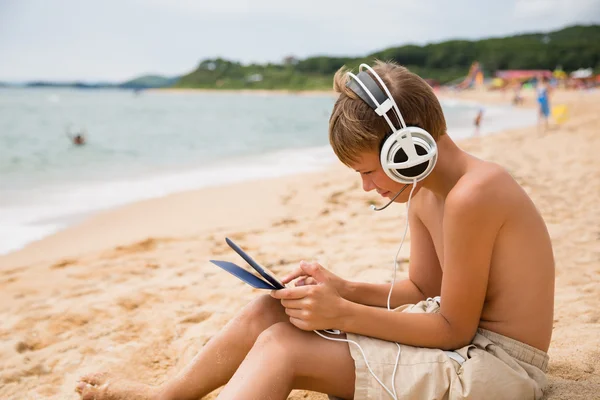 Boy playing Tablet PC sitting by sea