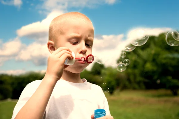 Boy inflates soap bubbles in summer park
