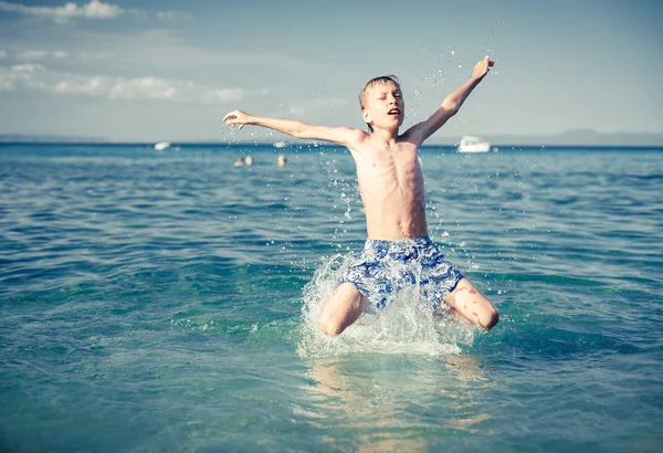 Funny little child playing in the sea splashing water and jumping. Summer vacation concept.
