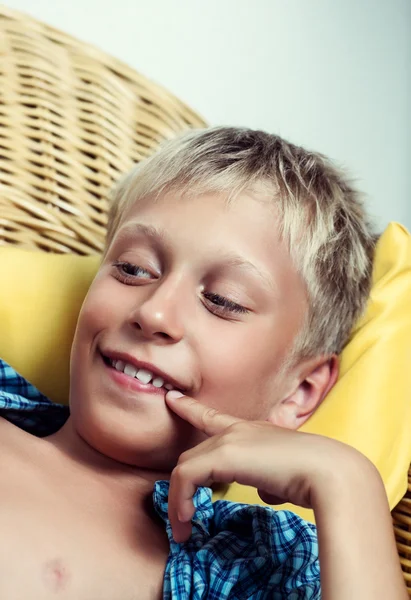 Beautiful funny little child lying on cozy wicker sofa dreaming and smiling.