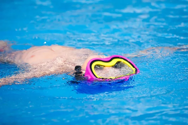 Child wearing a colorful swimming mask swimming in an open-air swimming pool