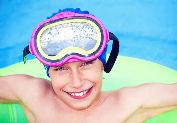 Cute funny child in a swimmer cap and mask swimming with yellow float in sea smiling