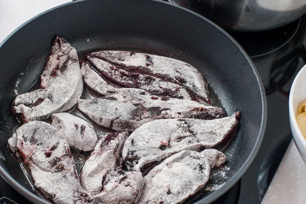 Cooking beef liver covered in flour on a frying pan.