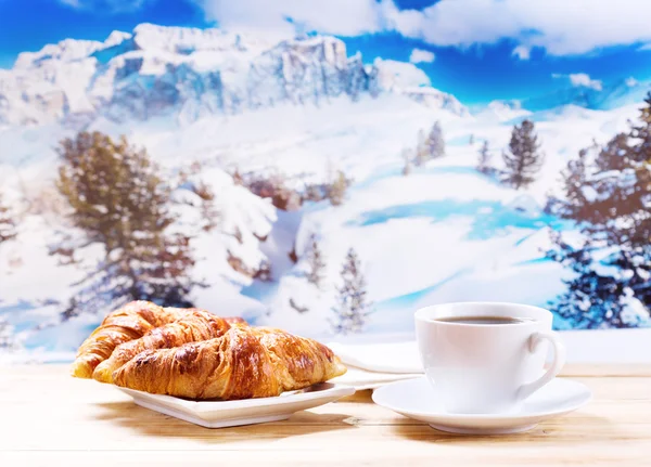 Cup of coffee and croissants over winter landscape