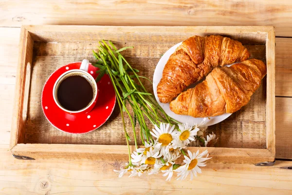 Breakfast tray with croissants, cup of coffee and daisy flowers