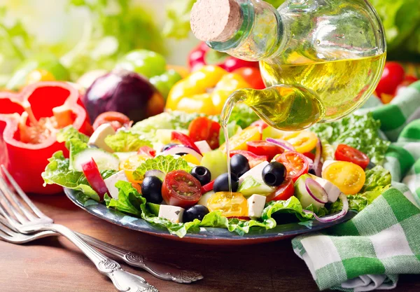 Olive oil pouring into plate of greek salad