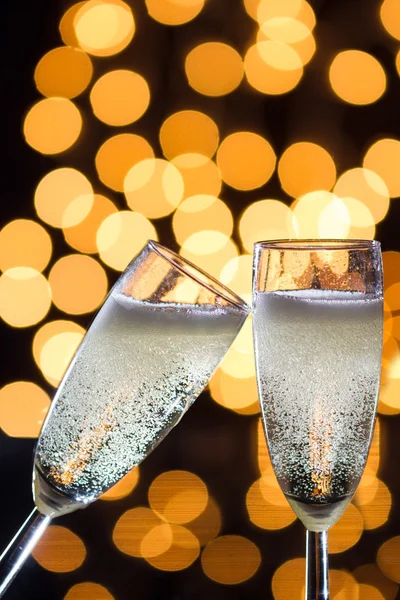 Two champagne glasses with bubbles and bokeh lights in the back
