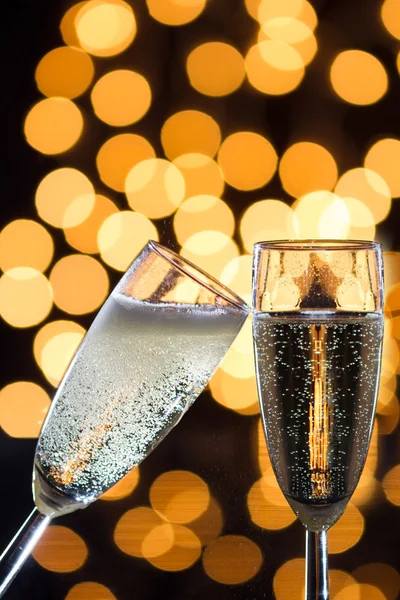 Two champagne glasses with bubbles and bokeh lights in the back