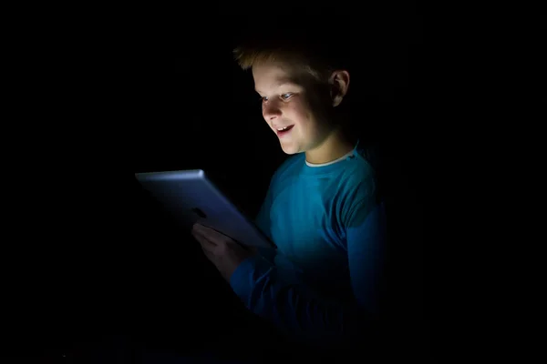 Young boy with light hair play with a tablet in dark