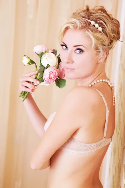Woman in beige lingerie with pearls and rose bouquet