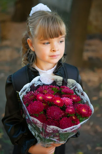 Schoolgirl with a bouquet of flowers in front of school