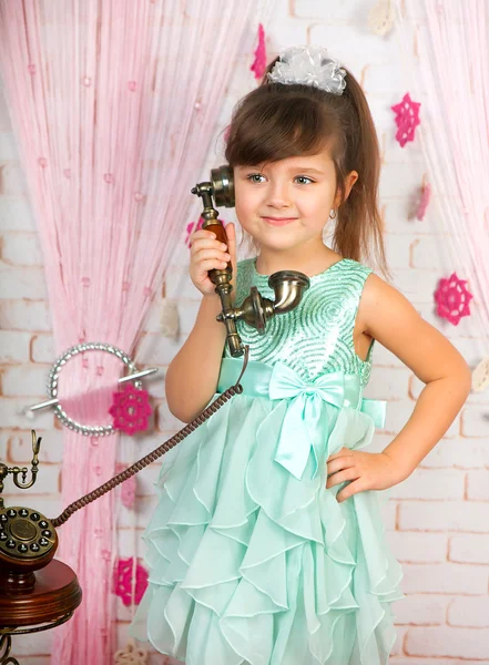 Little cute girl in a green dress is calling on an old phone in