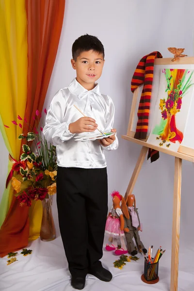 Little boy in a white shirt painting a picture on an easel in th