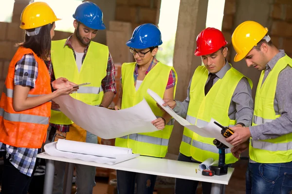 Group of architects and construction workers look at blue print