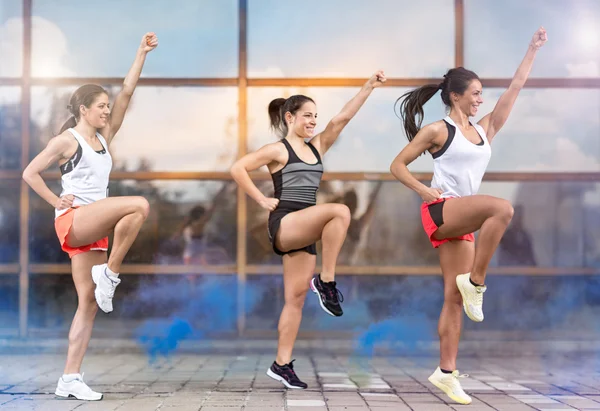 Three smiling girls doing aerobic exercises outside