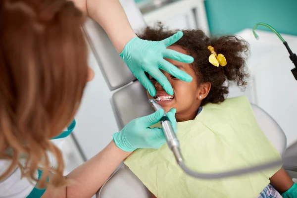 Female dentist polishing teeth to young girl