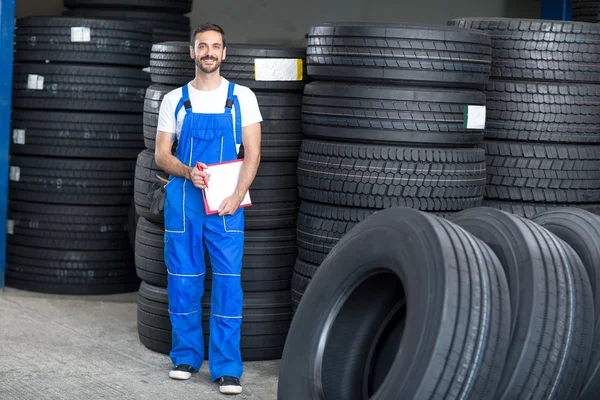 Smiling mechanic checing clipboard car tires