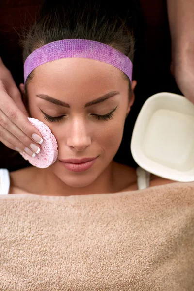 Beautician cleaning face of young female