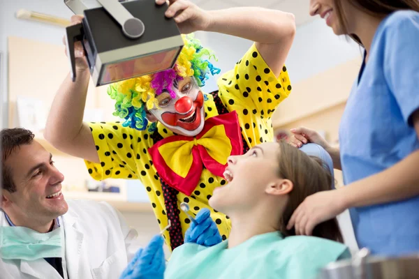 Clown in colorful clown suit make laugh young girl in dental amb