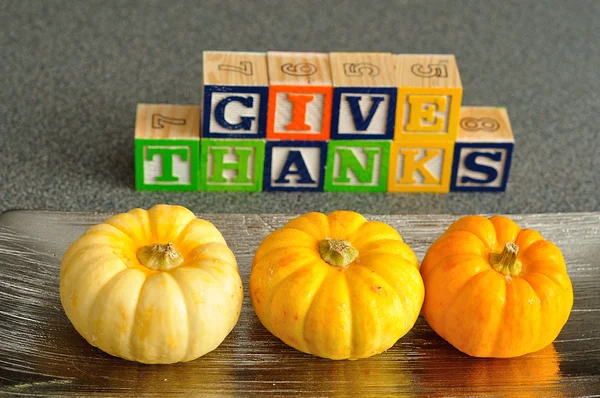 Pumpkins with Give thanks spelled with Alphabet blocks out of focus