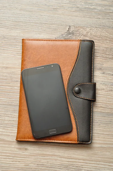 A notebook displayed with a smart phone on a wooden table