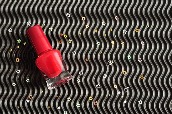 A red bottle of nail polish displayed on a black background