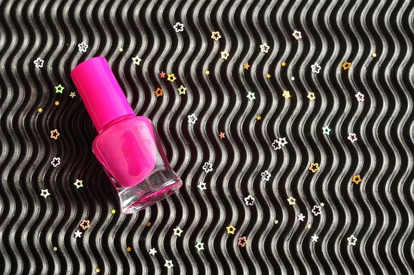 A pink bottle of nail polish displayed on a black background