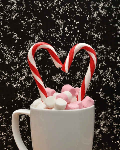 A mug filled with small marshmallows with two candy canes