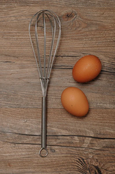 An egg beater, whisk, with two eggs
