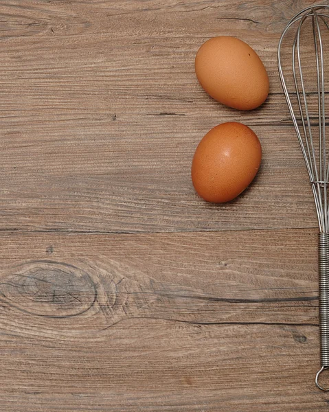 An egg beater, whisk, with two eggs