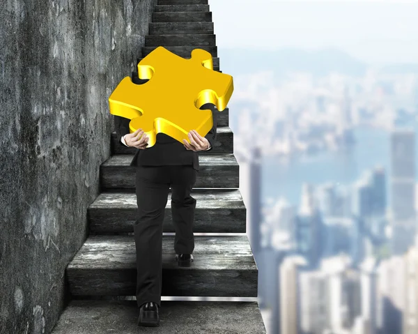 Businessman carrying gold puzzle piece climbing on old stairs