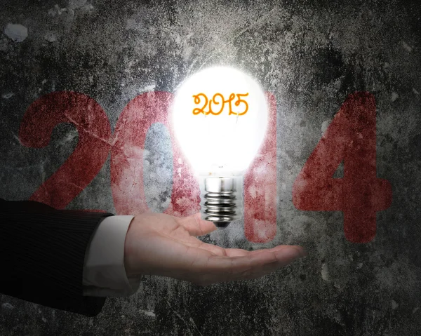 Hand holding brightly 2015 light bulb illuminated old concrete w