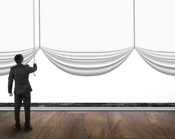 Businessman pulling open blank curtain with empty white backgrou