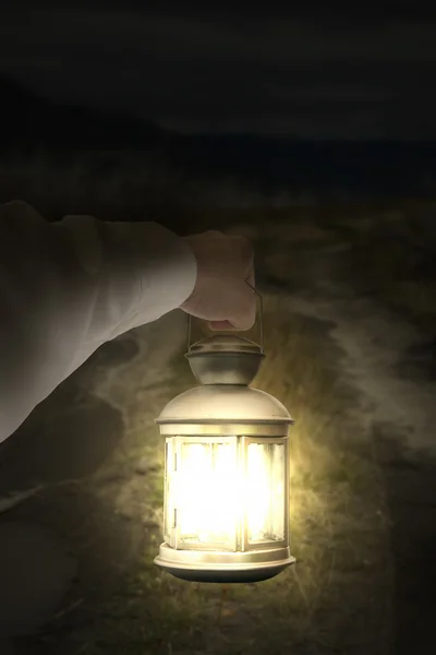 Left hand holding light illuminating dark road at night