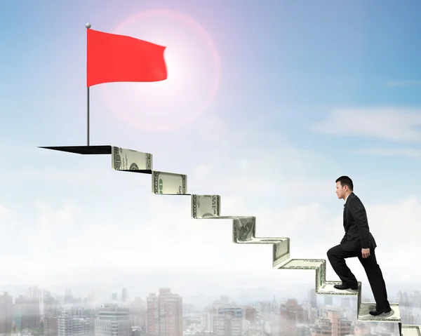 Side view businessman walking on money stairs to red flag