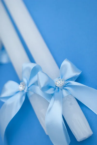 White wedding candles with blue ribbon decoration on the blue background