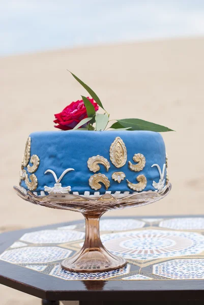 Blue wedding cake on a table and red roses on top in the desert landscape